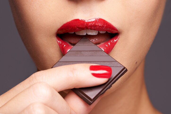 Closeup of a cute young female biting into a piece of chocolate