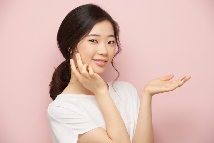 Smiling Korean girl applying moisturizer on her face