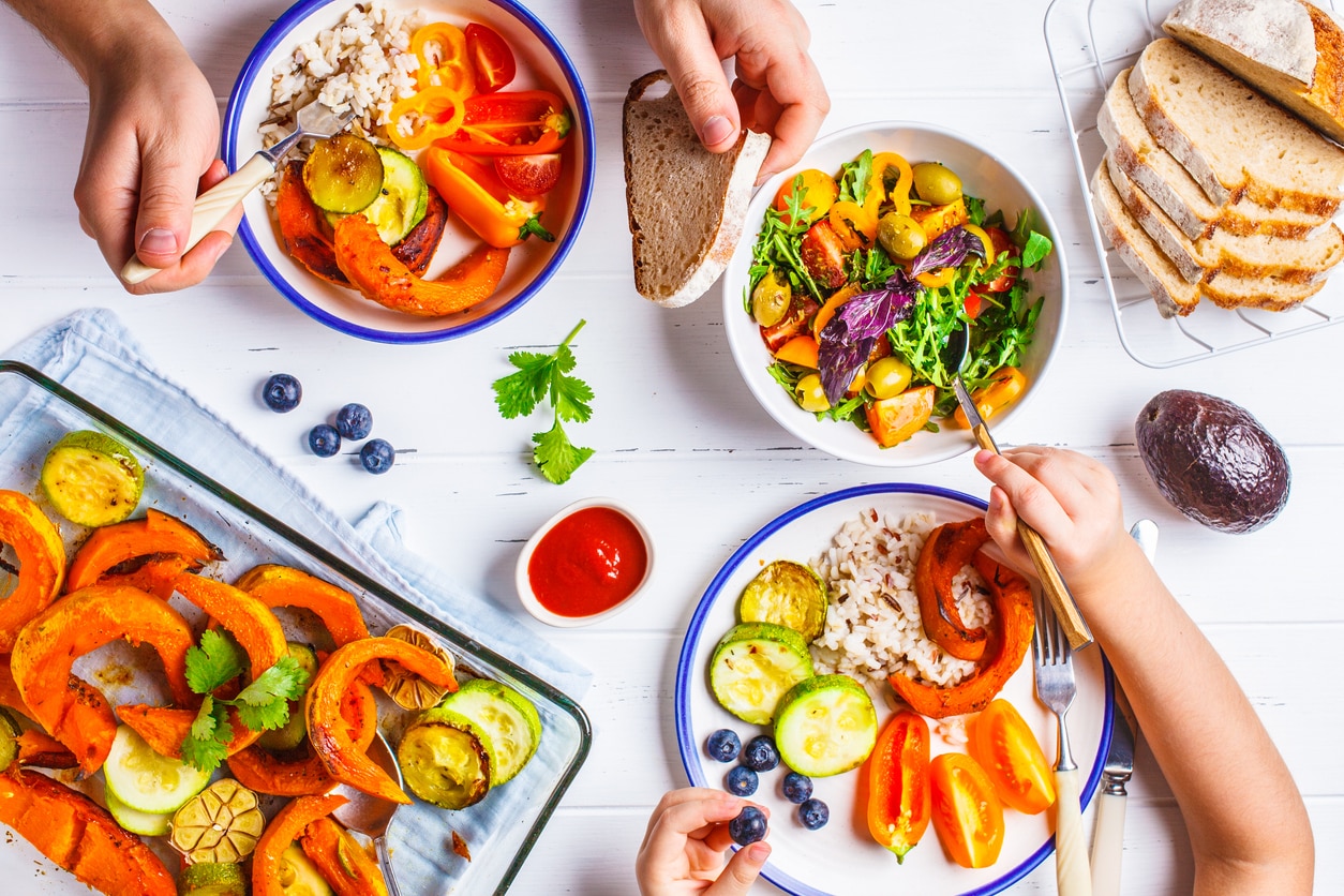 Flat lay of family hands eating healthy food. Vegan lunch table top view. Baked vegetables, fresh salad, berries, bread on a white background.