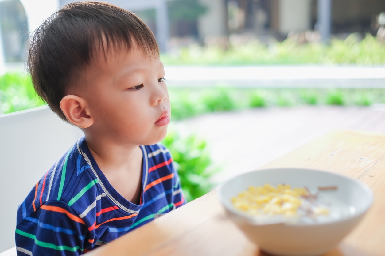 Asian toddler boy child wearing striped t shirt refuse to eat food, Little unhappy kid with no appetite bored of cereal as breakfast,  Child doesn't want to eat, Picky eater needs vitamins supplments