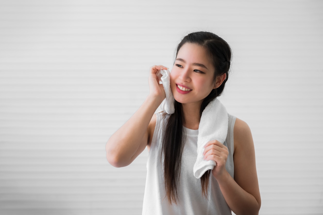 Portrait of happy beautiful asian woman using white towel wiping sweat from her face after exercise in home. Close up of healthy female or sports girl smile and wiping sweat with towel after workout.