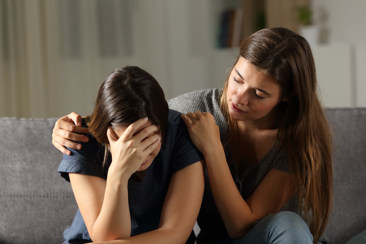 Teen comforting her sad friend in the night sitting on a couch in the living room at home