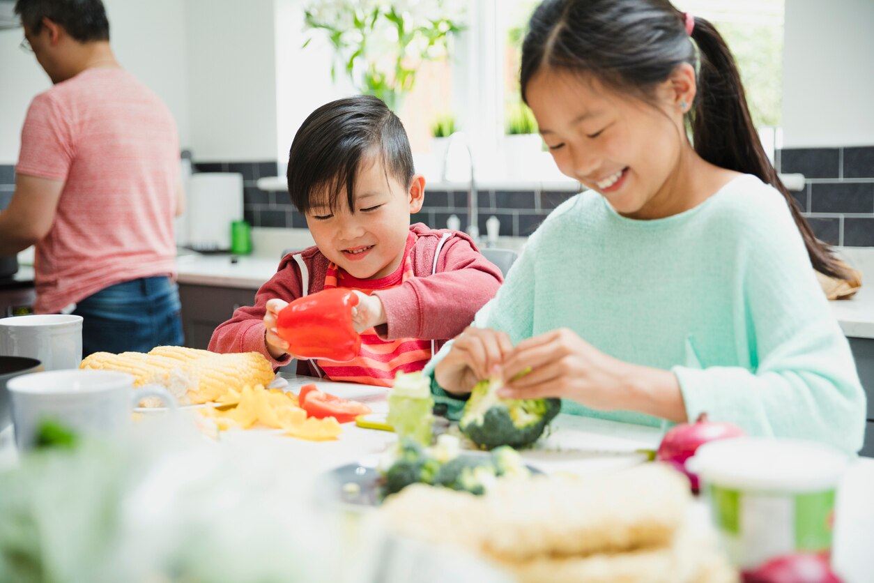 Little girl and her brother are helping their family to prepare a stir fry dinner. They are cutting up pepper and broccoli.