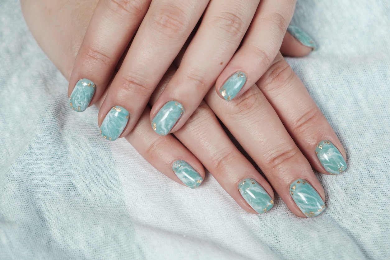 Model woman hand showing shellac marble green pastel manicure with gold leaf on short nails