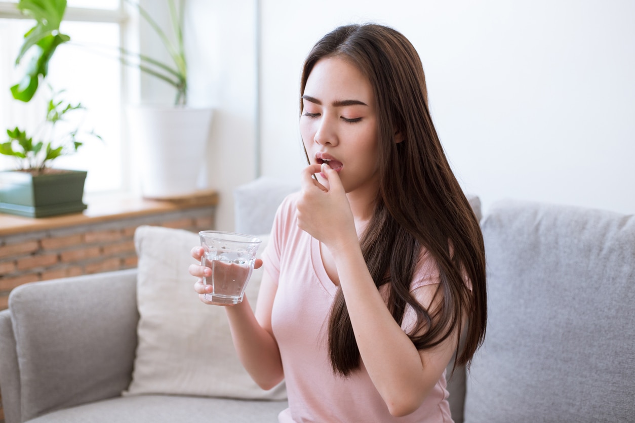 urinary tract infections cabn be treated with a short course of antibiotics. Sick young woman taking pills while sitting on the sofa at home