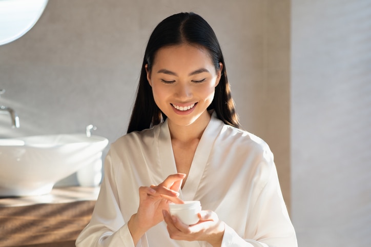 Smiling attractive young asian lady in white bathrobe holding jar with beauty product, enjoying morning routine for beautiful face skin, MBTI 16 Personalities – The best skincare gift for ISTP